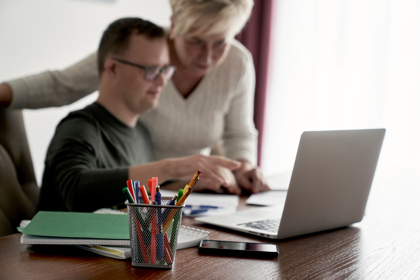 Selective focus of caucasian man with down syndrome studying with his mum at home